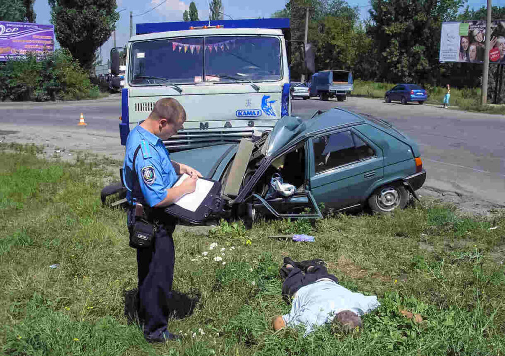 Houston police documenting evidence at a car crash site with damaged vehicle and injured person on grass.