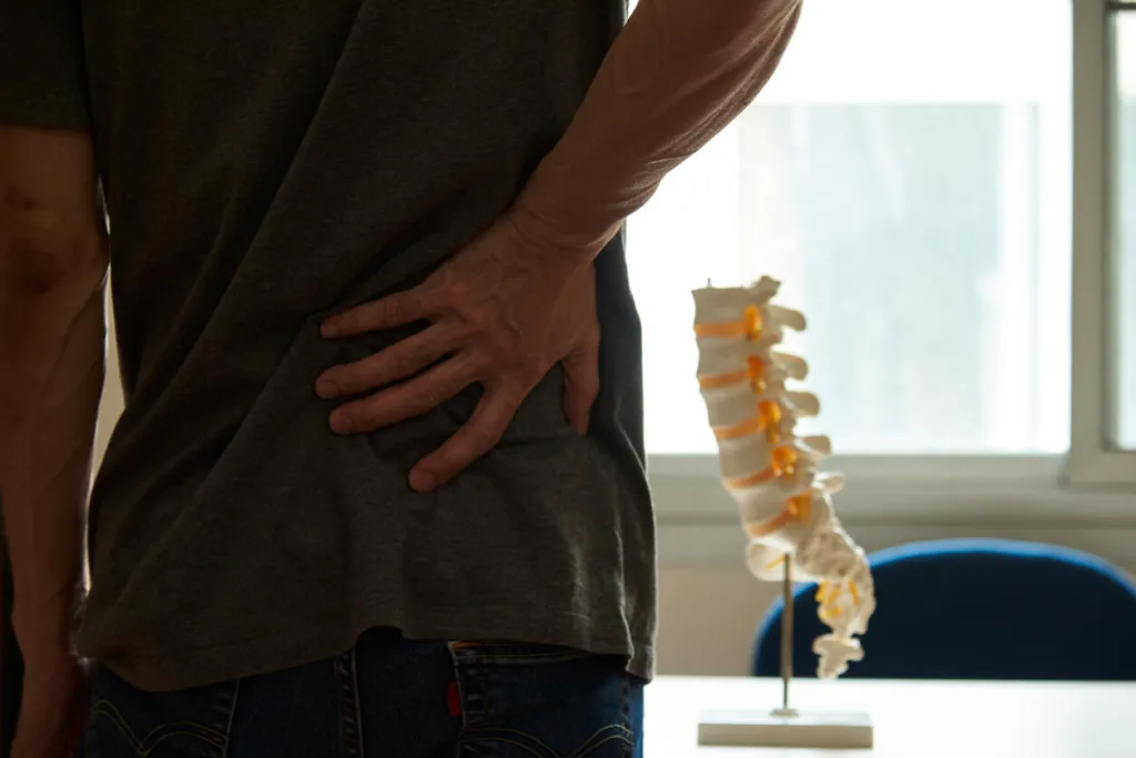 Man holding lower back in pain next to a medical model of human spine, illustrating herniated disc injury claim for Houston personal injury attorney assistance.