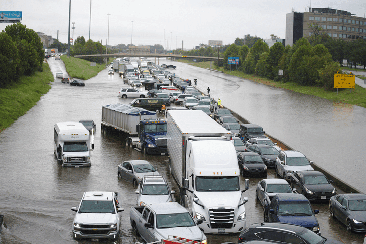 Flooded Houston highway with multi-vehicle pileup and stranded trucks, illustrating accident delays and complex liability issues