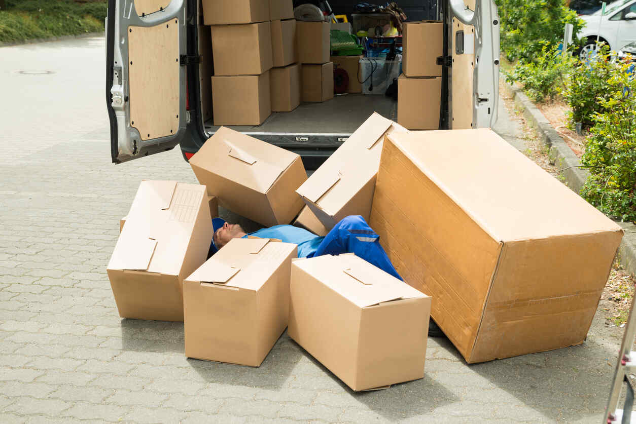 A delivery person is shown lying on the ground, surrounded by fallen cardboard boxes that have spilled out of the back of a delivery truck.