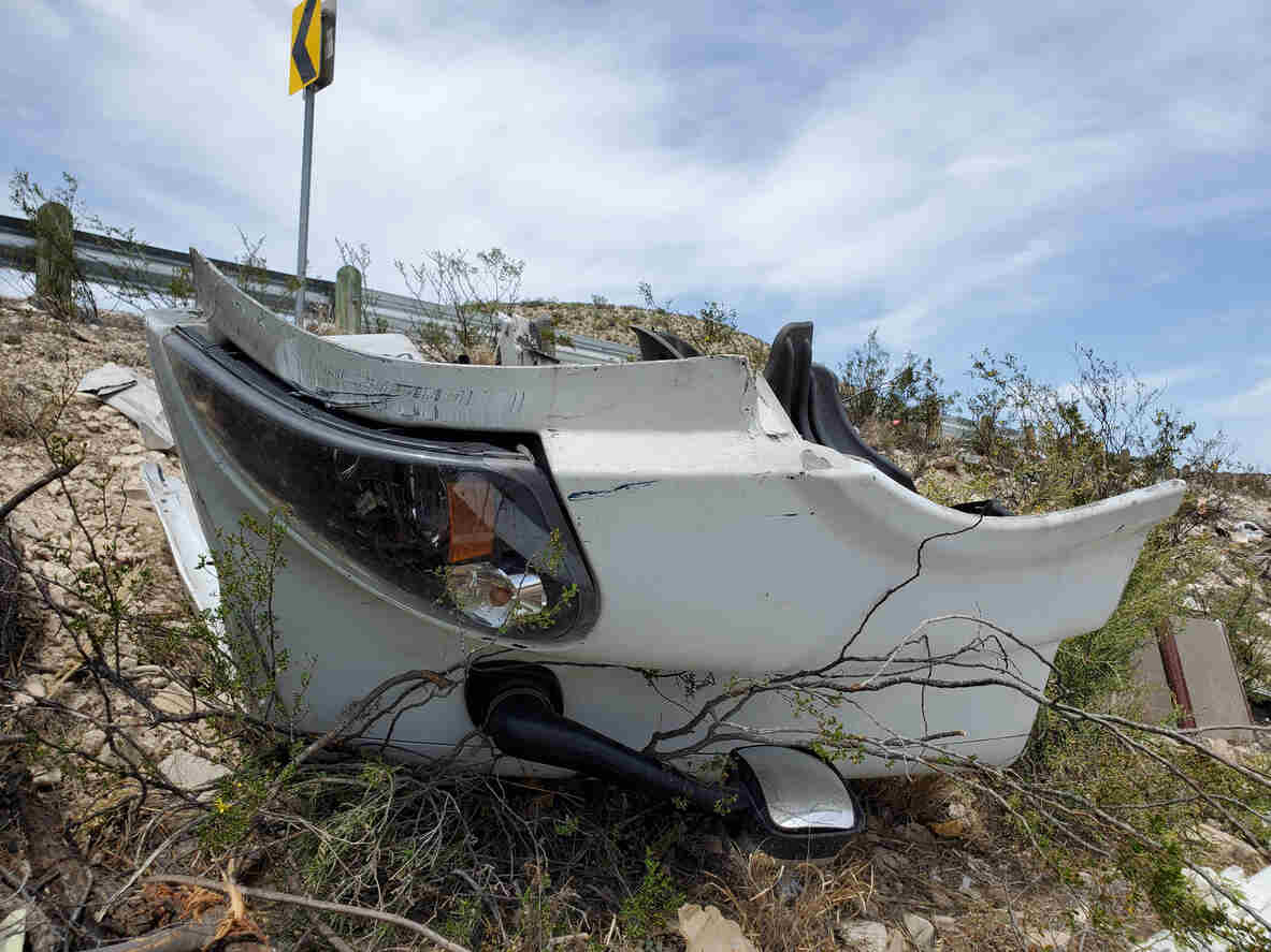 Wreckage from a vehicle collision scattered in a rugged, arid landscape, indicating a serious accident in a remote area like the Eagle Ford Shale.