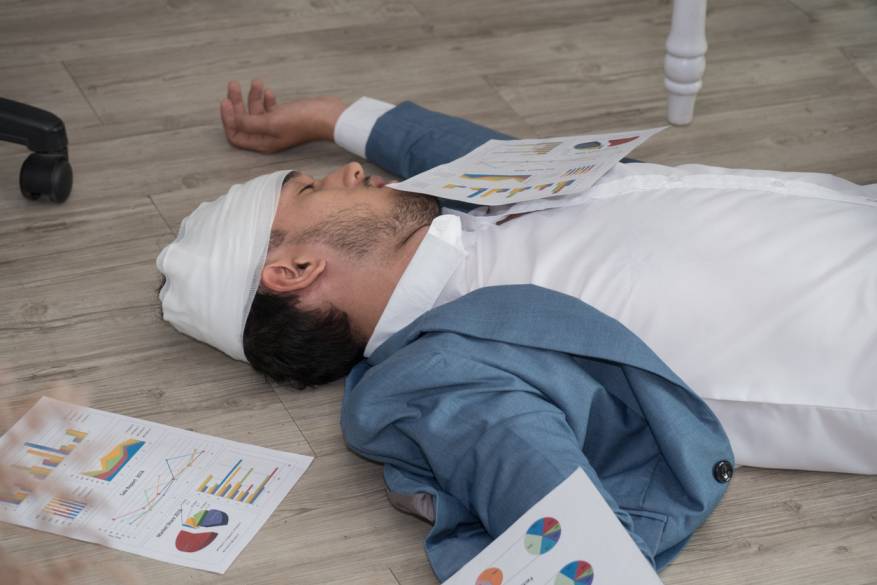 Business professional lying unconscious on the floor with head injury, surrounded by scattered charts and documents, illustrating a catastrophic injury scenario